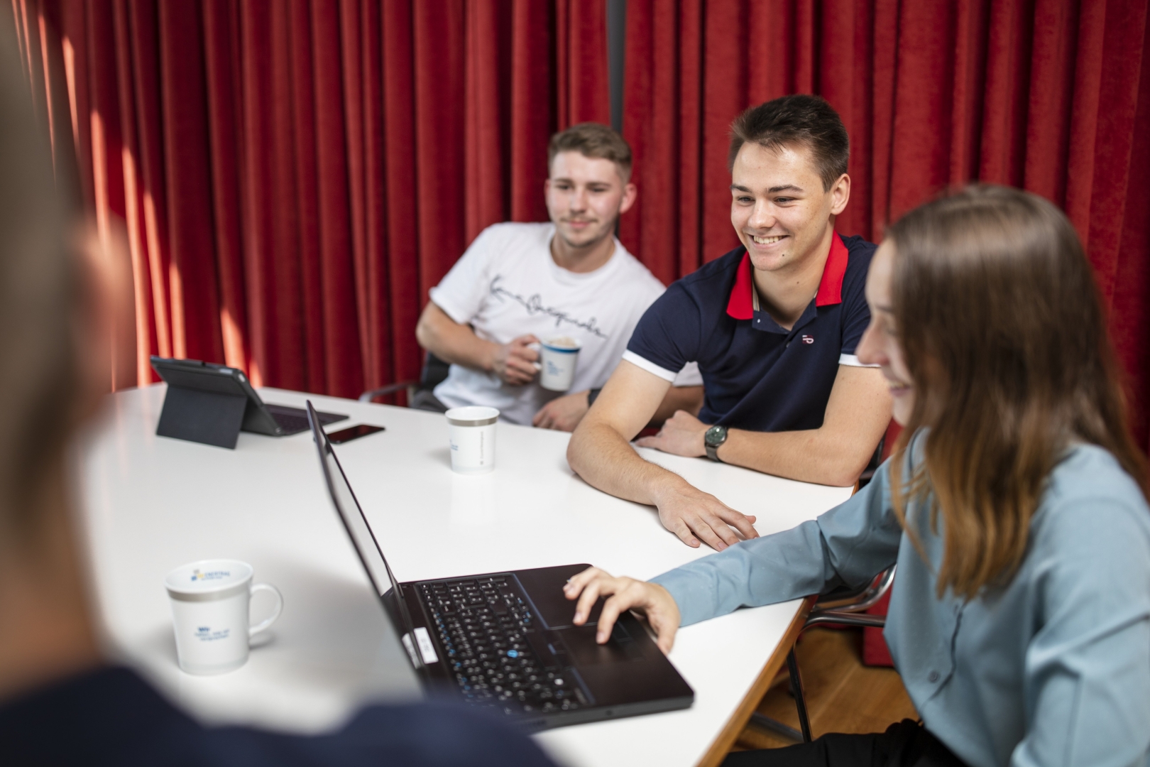3 Personen, die an einem Tisch sitzen und auf einen Laptop schauen
