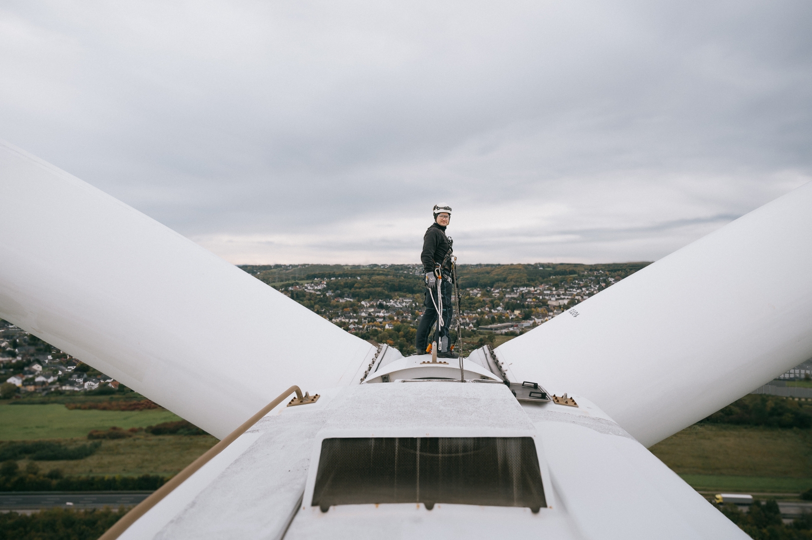 Servicetechniker steht auf einer Windenergieanlage mit Ausblick auf die Landschaft