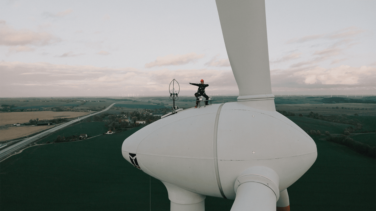 A service technician on top of a wind turbine, posing for a picture